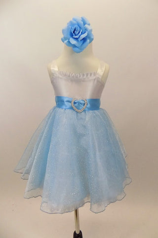 White satin bodice dress has front ruffle. Sparking blue organza rests over blue tulle. Wide blue satin waist sash has crystal heart accent. Has rose hair clip. Front
