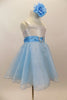 White satin bodice dress has front ruffle. Sparking blue organza rests over blue tulle. Wide blue satin waist sash has crystal heart accent. Has rose hair clip. Right side