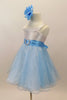 White satin bodice dress has front ruffle. Sparking blue organza rests over blue tulle. Wide blue satin waist sash has crystal heart accent. Has rose hair clip. Left side