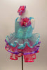 Pale aqua sequined dress has ruffled straps & pink-purple floral accent at left shoulder. Skirt has 3 tiers of pastel ruffles & matching hair accessory. Left side