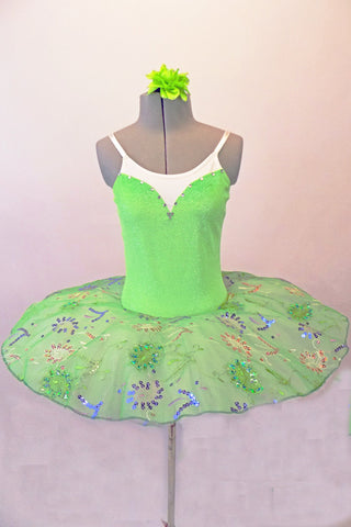 Delicate pale apple green tutu has a white pleated six-layer platter with the attached bodice and overlay. The sparkly green faux sweetheart cut is lined with crystals over a white camisole-style bodice. The sheer sequined lace overlay creates a really pretty soft look. Comes with a green floral hair accessory. Front