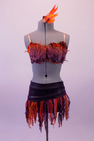 Exotic two-piece costume is a black scale-like bra covered at the front entirely by purple and orange feathers and adjustable nude straps. The matching skirt has an asymmetrical matching black waistband with orange and purple curly finger fringes. Comes with matching feather hair accessory. Front