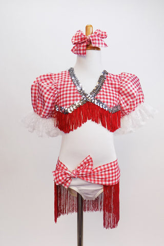 White leotard has red-white checkered bust area,  pouf sleeves with lace,  silver sequins and red fringe. Has checkered hip wrap with red fringe & hair bow. Front