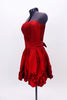 Red strapless taffeta dress has pleated front waist band & smocked back. Bottom of the dress is scalloped with rosettes.Has wide sash that  ties at the back. Side