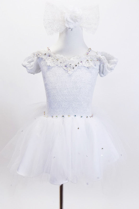 White lace leotard has attached crystal covered tutu skirt  & drop shoulder sleeves. Neckline has bridal lace with beads & pearls. Has hair accessory with veil. Front