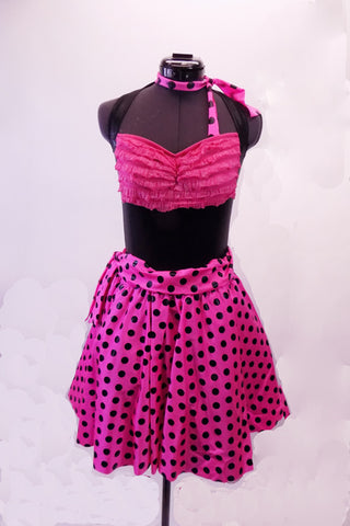 Black shiny halter leotard has a pink finely ruffled bust area. It is accompanied by black Capri leggings with a polka dot bow tie-up waistband. The matching polka dot knee-length skirt goes over the pants. Comes with matching neck scarf.  Front with skirt