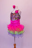 Rainbow sequined camisole tank dress has black cross straps. The curly ruffled skirt is layers of bright pink, blue and green with a black edge. There is an organza rose at the left bust. Comes with a pink floral hair accessory. Left side