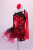 Red sequined short unitard has a black bust area angle & strapped in a unique angle with single red mesh long sleeve. The deep open back has three angled straps with a large sequined red and black floral accent. A large red and black tulle side pouffe accents the right hip. Comes with a red floral hair accessory. Left side