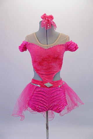 Bright pink, lined, sparkled half top dips down at the front to attach to the bottom. The top has a nude mesh upper to create the off-shoulder look. The attached lined short is a ruffled crepe with glitter & a large crystal buckle accessory. There is an attached tulle bustle skirt. Comes with a bow hair accessory.  Front