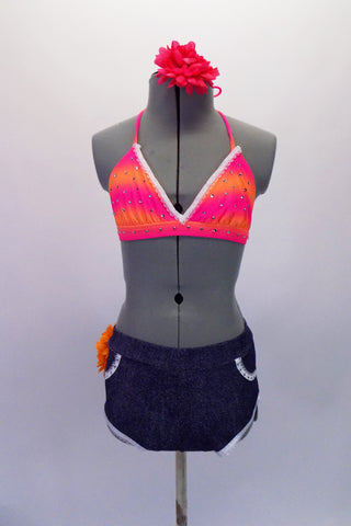 Two-piece costume is faux denim shorts with a delicate thin white lace trim on legs and pockets. There is a large orange flower at the back of the right hip. The matching triangle bikini top is neon pink and orange and scattered with clear Swarovski crystals. Comes with matching pink floral hair accessory. Front