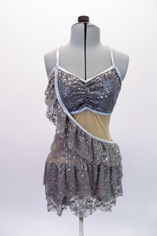 Silver lace sequined leotard has a nude mesh centre and pinched bust. The attached short flounce skirt is a layer of nude mesh covered by silver lace. The uniqueness of the dress comes from the sash like ruffled lace overlay that crosses over the right side. Comes with a silver hair accessory. Front