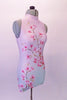 Short halter style unitard with high collar and open back has a cherry blossom pattern that cascades from the right shoulder to the left hip in a soft shade of blush pink and mint green. Right side