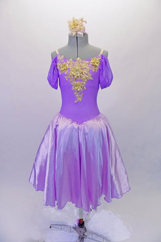 Beautiful lavender romantic ballet dress has a calf-length satin circle skirt over layers of tulle. The bodice is a lavender camisole with elastic straps and cold-shoulder style sleeves. The bust is adorned with a large 3-D gold floral applique that really makes a statement. Comes with a gold applique hair accessory. Front