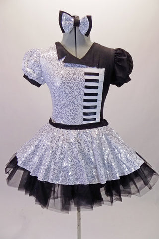Piano themed dress is silver sequined on right side of bodice & skirt overlay. The left side, single lapel collar & petticoat are black. The costume has colour matched pouffe sleeves. A piano keyboard is appliqued on the left side of the torso. The back is looped with a silver bow. Comes with a bow hair accessory.
