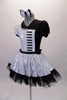 Piano themed dress is silver sequined on right side of bodice & skirt overlay. The left side, single lapel collar & petticoat are black. The costume has colour matched pouffe sleeves. A piano keyboard is appliqued on the left side of the torso. The back is looped with a silver bow. Comes with a bow hair accessory. Left side