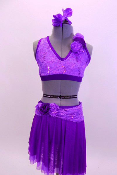 Two piece costume comes with purple sequined lace halter half top. The back has crystal covered straps with crystal ring accent.  The skirt has layers of darker purple mesh with lighter matching lace accent around hip. Both pieces have lace rose accents on left shoulder and right hip. Comes with floral hair accessory. Front