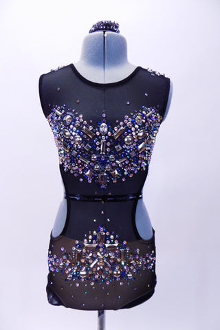 Black mesh leotard with open sides and back is lined with nude lycra in brief area. The costume is extensively covered with jewels, Swarovski crystals and metal studs along the bodice and hips.  Comes with metallic jewel hair accessory. Front