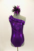 Purple metallic one-shoulder leotard has ruffle accent with crystals. Torso has sequined braiding & large jeweled applique. Comes with feathered hair accessory. Front