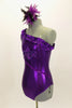 Purple metallic one-shoulder leotard has ruffle accent with crystals. Torso has sequined braiding & large jeweled applique. Comes with feathered hair accessory. Left side
