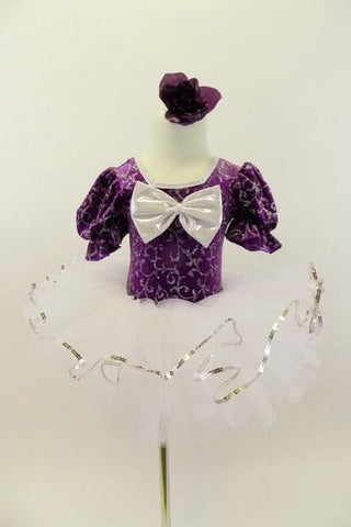 Purple velvet leotard has pouf sleeves & silver pattern. Neck-line is square cut with silver edging & large silver front bow. Comes with white pull-on tutu & floral hair accessory. Front