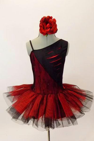 Red and black tutu dress has one shoulder & angled bodice with slits/cuts into black half to reveal red beneath. Tutu is crisp red tulle overtop of black. Has red floral hair accessory. Front