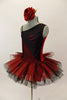Red and black tutu dress has one shoulder & angled bodice with slits/cuts into black half to reveal red beneath. Tutu is crisp red tulle overtop of black. Has red floral hair accessory. Left side