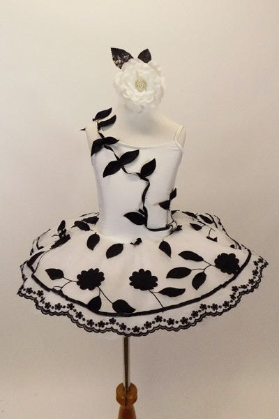 White pancake tutu has cascading black 3-D leaves on a vine of black ribbon. Overlay has black flowers & scalloped floral lace trim. Has matching hair accessory. Front