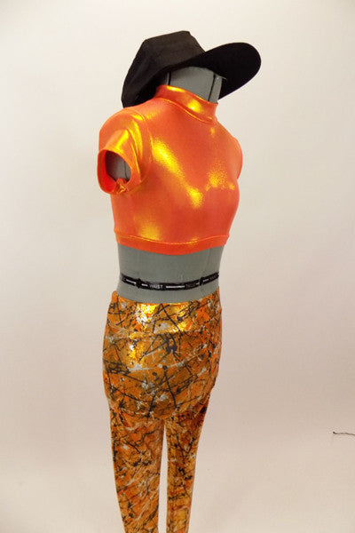 Bright orange metallic high neck half top has keyhole back. Accompanied by metallic orange leggings with a black & silver splatter pattern & black baseball cap. Left side