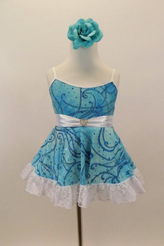 Camisole leotard dress has swirls of blues on aqua base. Has a white petticoat and wide lace trim. White satin waist sash had a crystal heart. Has floral hair accessory. Front