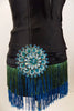 Roaring 20s style costume has bodice with lace bra & green-turquoise fringe. Black briefs have the matching fringe and a huge round crystal brooch at hip. Has turquoise feather hair piece. Brooch zoomed