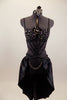 Black crystal covered bra is attached to bottom by a series of straps that converge to a point. Shorts have front chain detail under an open front satin skirt. Front