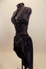 Black crystal covered bra is attached to bottom by a series of straps that converge to a point. Shorts have front chain detail under an open front satin skirt. Lef side