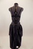 Black crystal covered bra is attached to bottom by a series of straps that converge to a point. Shorts have front chain detail under an open front satin skirt. Back