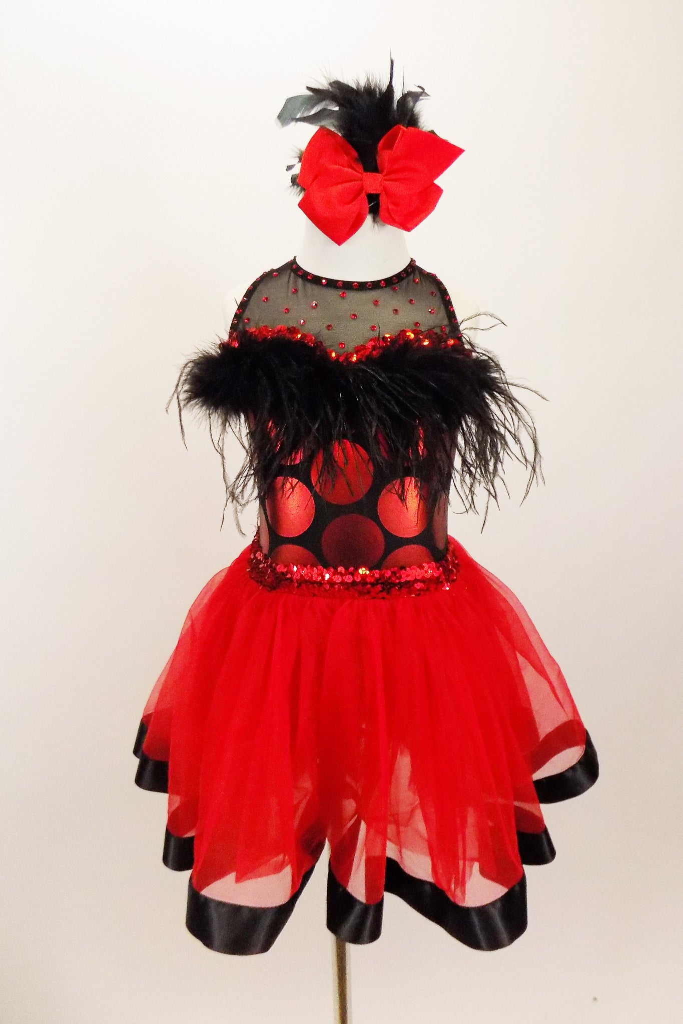 Dress has bodice with sweetheart neck polka dots & black mesh covered with crystals & feather trim. Skirt is red tricot with black satin hem. Has hair accessory. Front