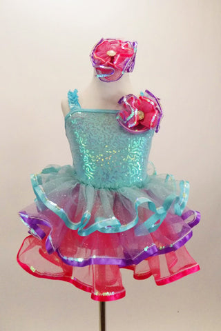 Pale aqua sequined dress has ruffled straps & pink-purple floral accent at left shoulder. Skirt has 3 tiers of pastel ruffles & matching hair accessory. Front