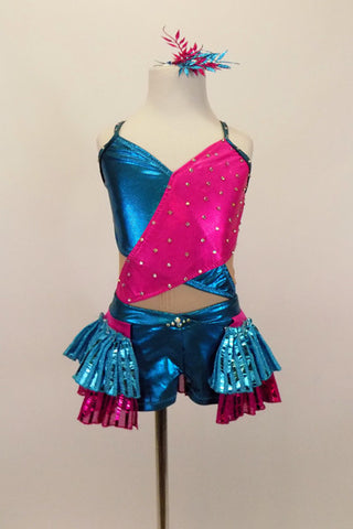 Nude mesh base leotard has metallic fuchsia-turquoise cross over front with crystals.  Shorts have layers of pleated ruffles. Comes with matching hair accessory. Front