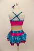 Nude mesh base leotard has metallic fuchsia-turquoise cross over front with crystals.  Shorts have layers of pleated ruffles. Comes with matching hair accessory. Back