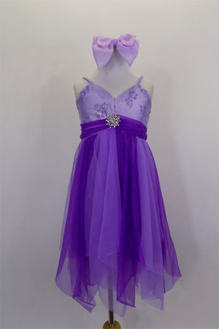 Lavender & purple A-line dress has empire waist & spaghetti straps. There are purple & silver flowers on the bust & skirt is layers of mesh &  a gathered belt. Comes with lavender hair bow. Front