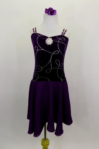 Dark purple velvet pinch front leotard dress has silver swirls on front torso with double cross straps are covered in crystals. Attached skirt is purple chiffon. Comes with hair accessory. Front