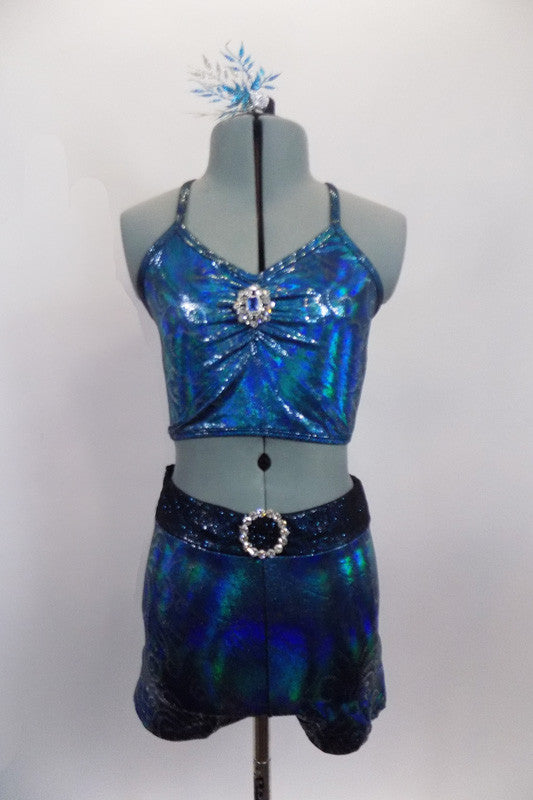 Turquoise iridescent, silver swirl two -piece costume has half top with cross back straps and crystal brooch accent. The matching shorts have a teal glittery waistband with crystal ring buckle accent. Comes with matching hair accessory. Front