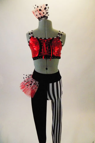 Funky 2-piece costume has a red sequined half top with front lacing & black and white striped piping & straps. The leggings are half black & half black-white vertical striped. Leggings have a red & black-white dotted hip ruffle on the right hip. Comes with matching ruffled hair accessory. Front