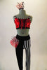 Funky 2-piece costume has a red sequined half top with front lacing & black and white striped piping & straps. The leggings are half black & half black-white vertical striped. Leggings have a red & black-white dotted hip ruffle on the right hip. Comes with matching ruffled hair accessory. Front
