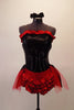 Black and red costume has a black bodice decorated with crystals with red ruffle along bustline that looks strapless but has clear shoulder straps. The lower back has laced corset accent over a red insert. The bottom is red shorts with black edged ruffles below an open front bustle skirt with red tulle and black overlay. Comes with matching crystaled gauntlets hair accessory. Front