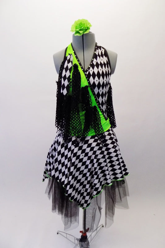 Black & white checkered harlequin themed dress has a lime green cross-over, halter bodice with attached black mesh kerchief accents cascading throughout. Swarovski crystals are scattered within the checkered pattern of the fabric that sits over layers of black tulle. Comes with a green floral hair accessory. Front