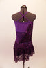 Plum cross-back short unitard base dress has purple mesh midriff & crystal accents along neckline. A purple sequin overlay is attached at right bust & cascades across front & back revealing leotard beneath. The sequin overlay acts as the skirt with a distinct plum waistband. Comes with floral hair accessory. Back