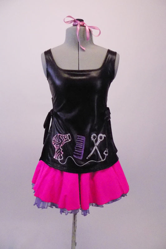 Hairdresser themed costume has black leatherette tunic style top with hand painted scissors, comb and blow drier. The tunic top ties at the sides and sits over top of a bright pink skirt with purple tricot petticoat. Comes with pink hairbow. Front