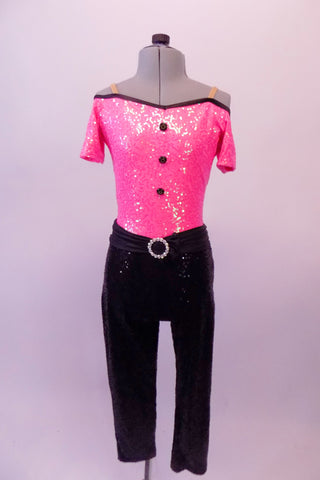 Fully sequined bright pink and black capri-length unitard is an off-shoulder top with black piping, cap sleeves, nude shoulder straps and black button accents. The attached black capri pat is a straight leg with gathered waistband and crystal ring buckle accent. Comes with a hair accessory. Front
