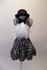 Black halter style dress has prominent silver swirled vine pattern. The neck has a large black bowtie from which cascades a large tulle layered ascot/bib. Comes with a black bowler hat. Front