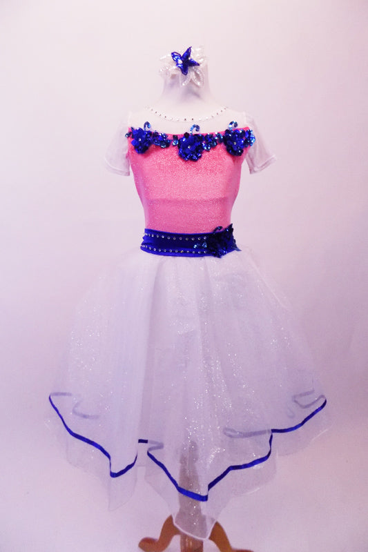 Romantic style ballet dress has pink glitter bodice with white crystal lined bust and cap sleeves. The bust and waist are embossed with royal blue 3-D sequined floral applique and large back bow. The attached white skirt is crystal-tulle with petticoat and trimmed with royal blue ribbon. Comes with a hair accessory. Front