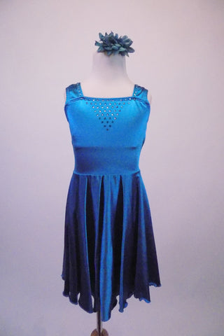 Soft, silky, flowing teal dress has knee-length lightly gathered circle skirt. The bodice has a triangular crystal accent and wide shoulder straps. Comes with a floral hair accessory. Front